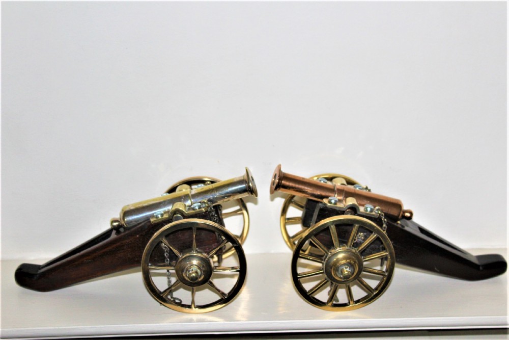 A pair of antique polished bronze desk cannons mounted on dark mahogany wooden carriages with brass spoked wheels. View II