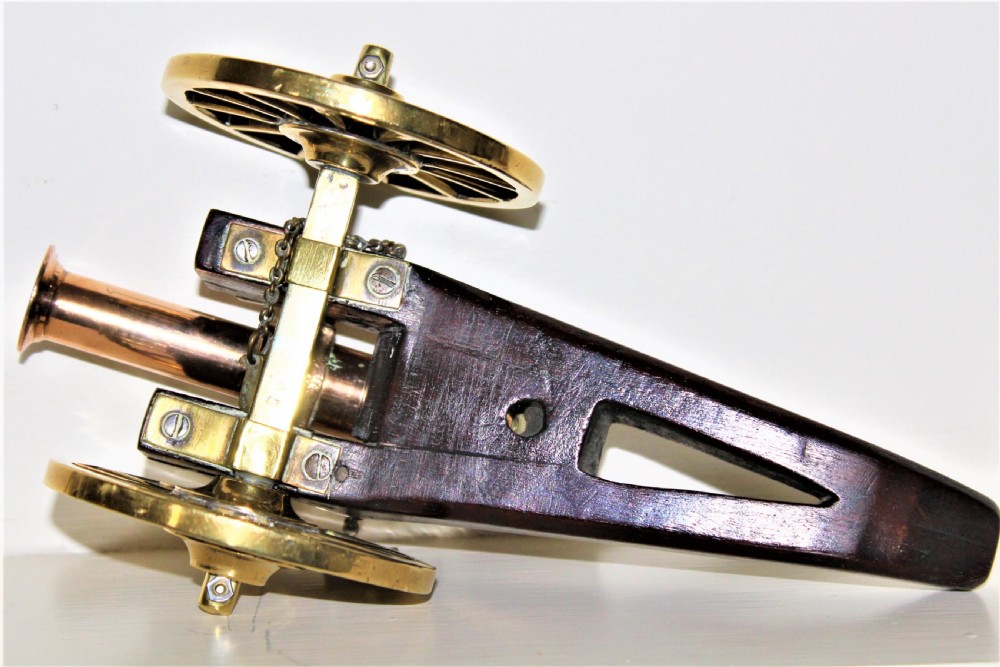A pair of antique polished bronze desk cannons mounted on dark mahogany wooden carriages with brass spoked wheels. View IV