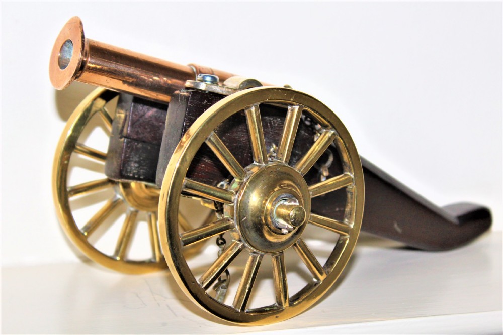 A pair of antique polished bronze desk cannons mounted on dark mahogany wooden carriages with brass spoked wheels. View V
