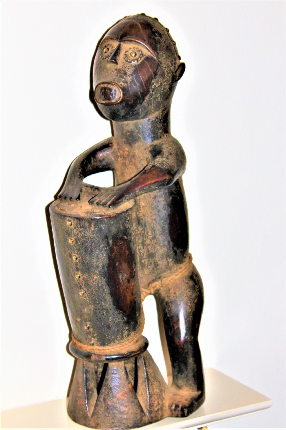 A well carved African tribal figure of a man beating a drum possibly by the Kongo people of west central Africa 