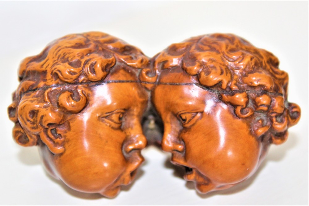 A carved boxwood brooch depicting two cherub heads in profile facing each other with detailed curly hair.