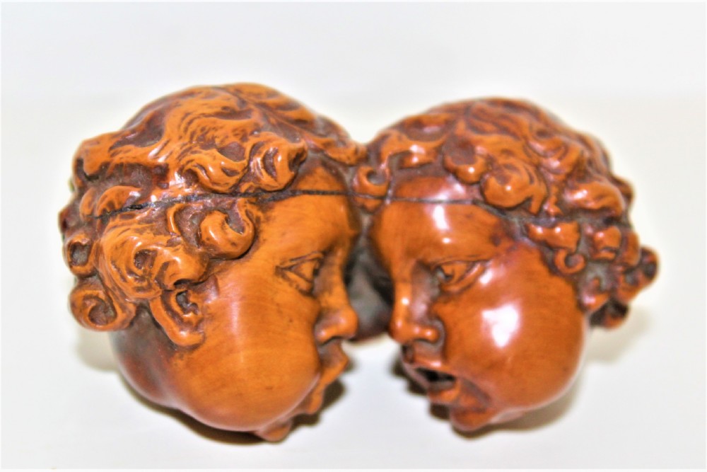 A carved boxwood brooch depicting two cherub heads in profile facing each other with detailed curly hair. View II