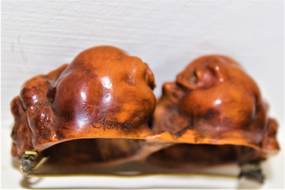 A carved boxwood brooch depicting two cherub heads in profile facing each other with detailed curly hair. View III