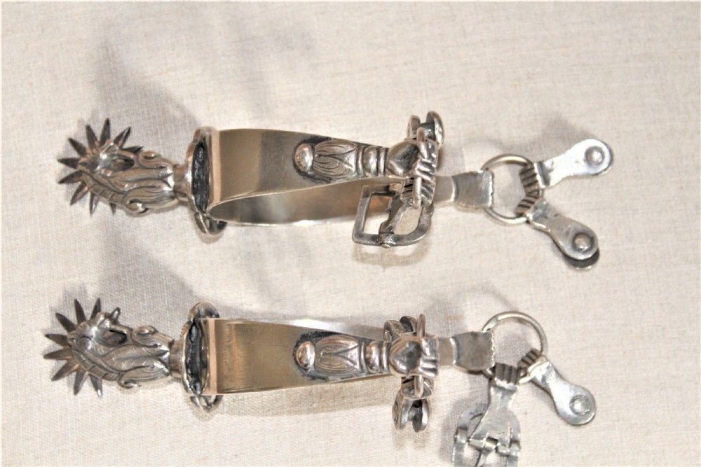 A pair of ornate late 19th-century South American metal spurs featuring multi-pointed starburst rowels and dangling charms. View V