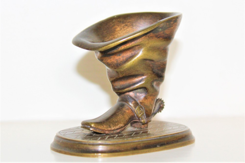 A 19th-century cast bronze paperweight shaped like a folded riding boot with a rowel spur on an oval engraved base.