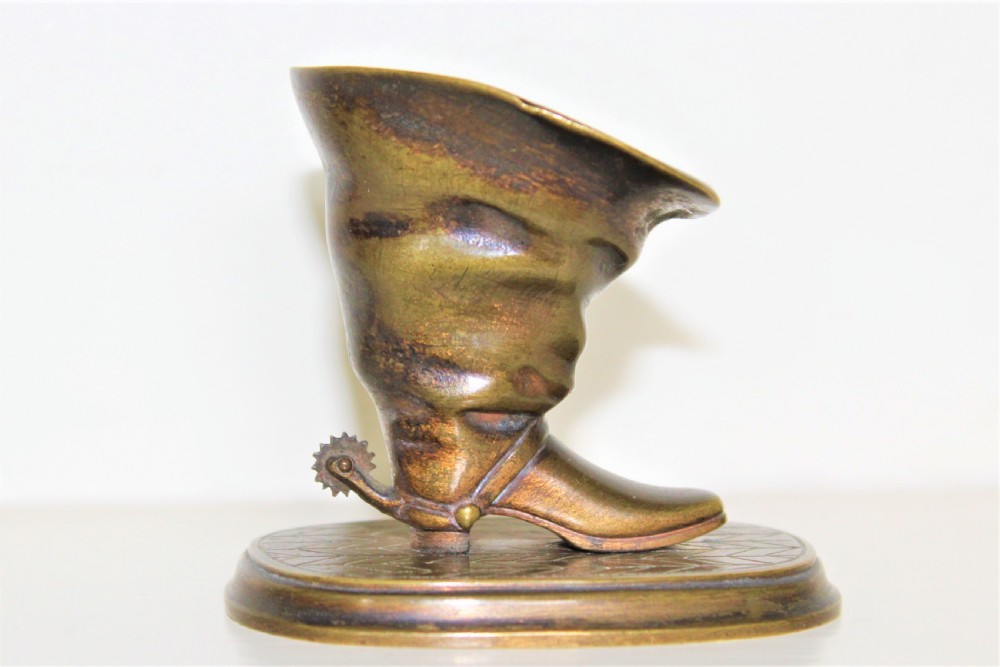 A 19th-century cast bronze paperweight shaped like a folded riding boot with a rowel spur on an oval engraved base. View II