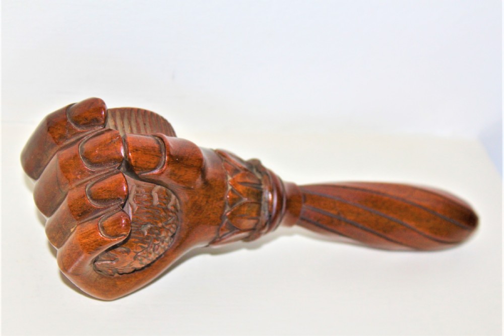 A late 19th-century carved brown wood nutcracker in the form of a clenched hand holding a nut.