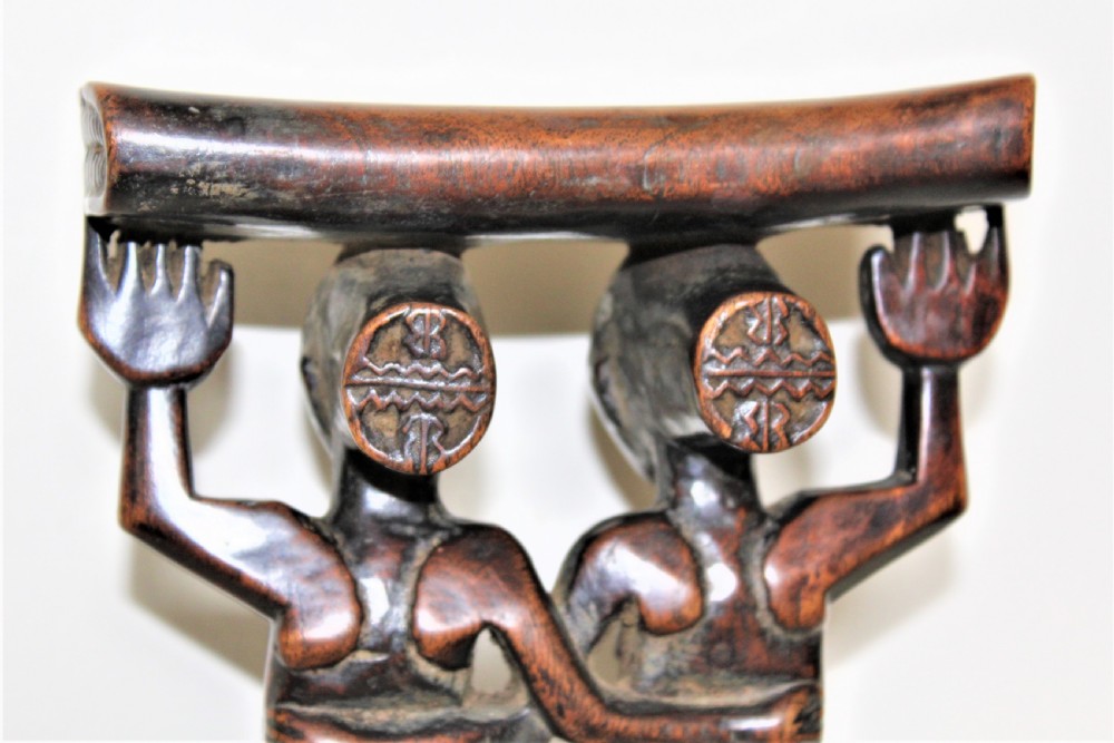 A carved dark hardwood headrest supported by two standing female caryatid figures on a circular carved base. View III