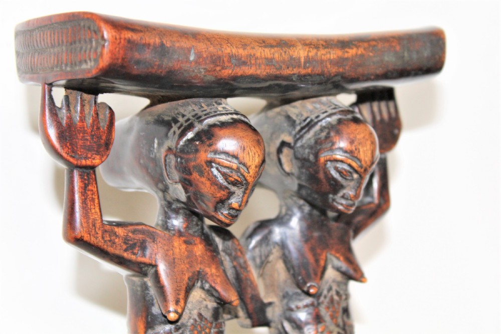 A carved dark hardwood headrest supported by two standing female caryatid figures on a circular carved base. View IV