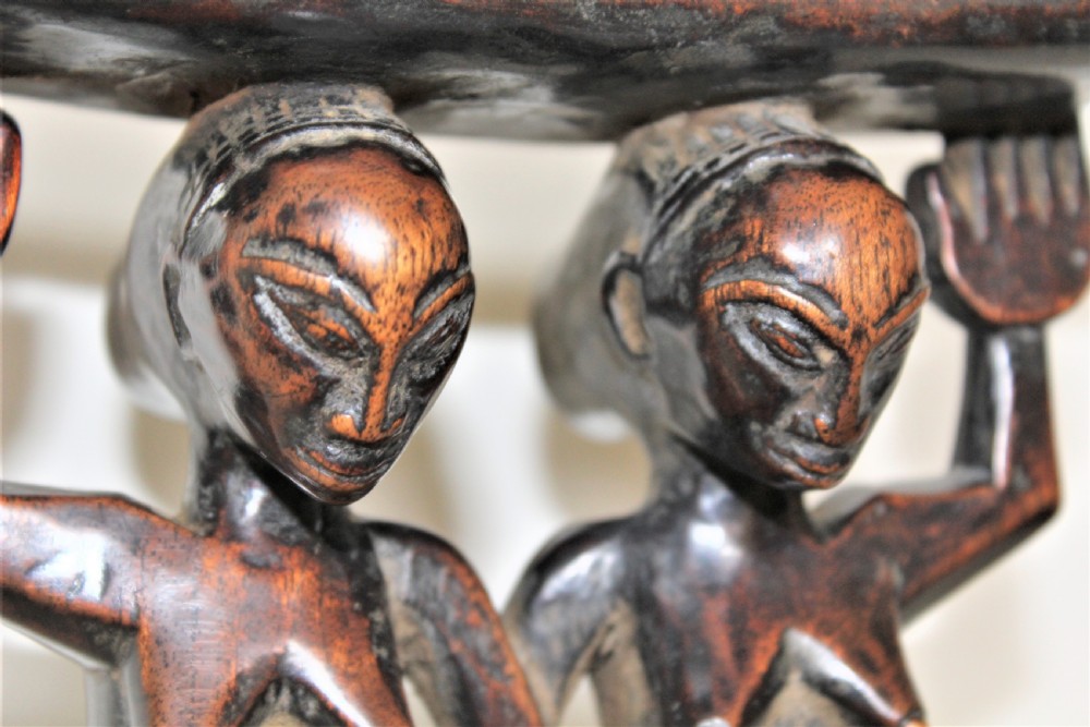 A carved dark hardwood headrest supported by two standing female caryatid figures on a circular carved base. View X