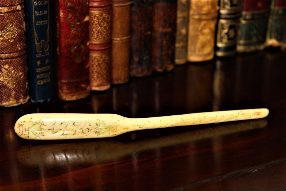 A hand-carved cream bone marrow spoon featuring an engraved date of 1776 and decorative foliage motifs along its handle.