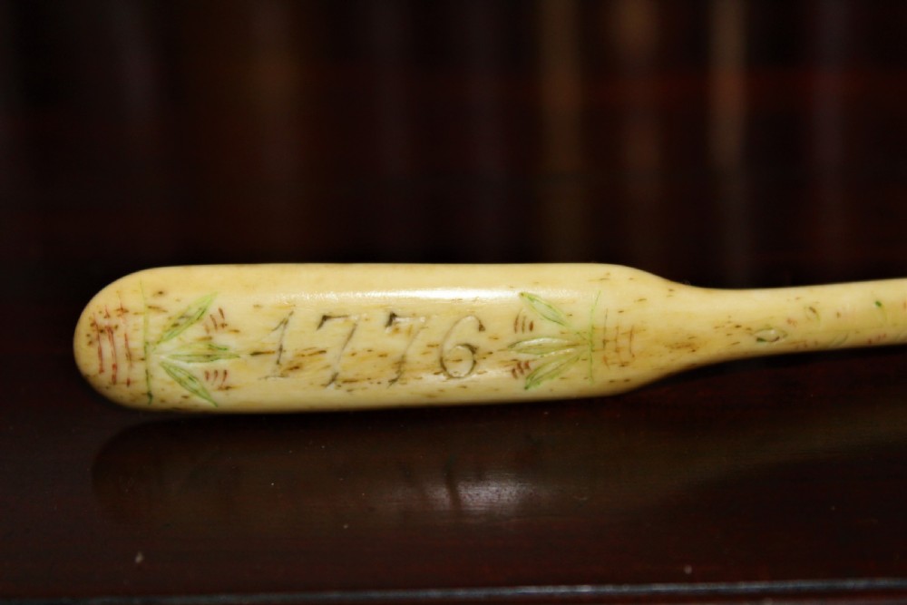 A hand-carved cream bone marrow spoon featuring an engraved date of 1776 and decorative foliage motifs along its handle. View II