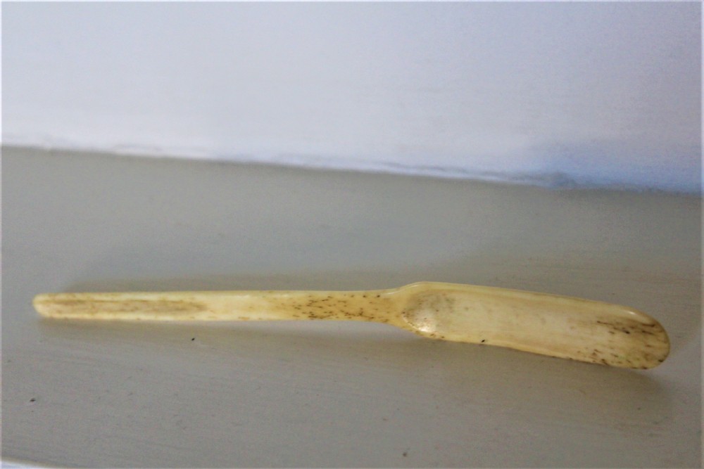A hand-carved cream bone marrow spoon featuring an engraved date of 1776 and decorative foliage motifs along its handle. View VI