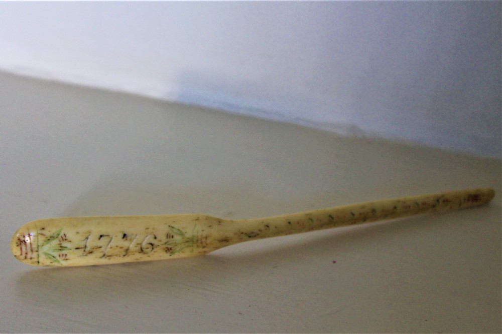 A hand-carved cream bone marrow spoon featuring an engraved date of 1776 and decorative foliage motifs along its handle. View VII