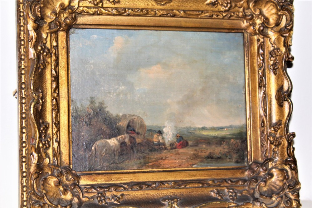 A small and charming well painted oil on panel depicting a couple sitting by a camp fire by a lake with a horse and wagon in the background 