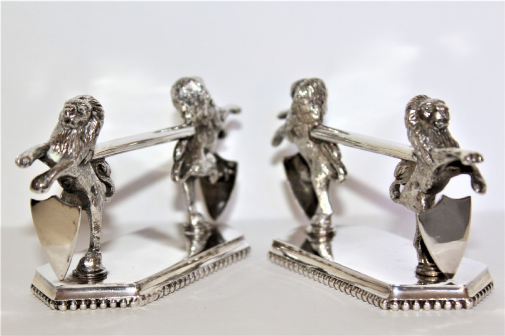 A pair of silver-plated knife rests featuring rampant lions holding shields mounted on beaded rectangular bases.