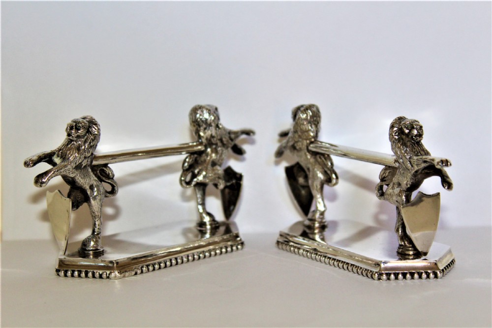 A pair of silver-plated knife rests featuring rampant lions holding shields mounted on beaded rectangular bases. View II