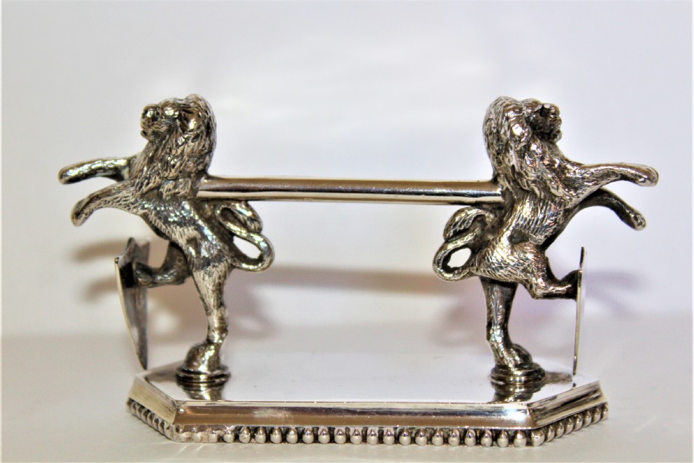 A pair of silver-plated knife rests featuring rampant lions holding shields mounted on beaded rectangular bases. View III