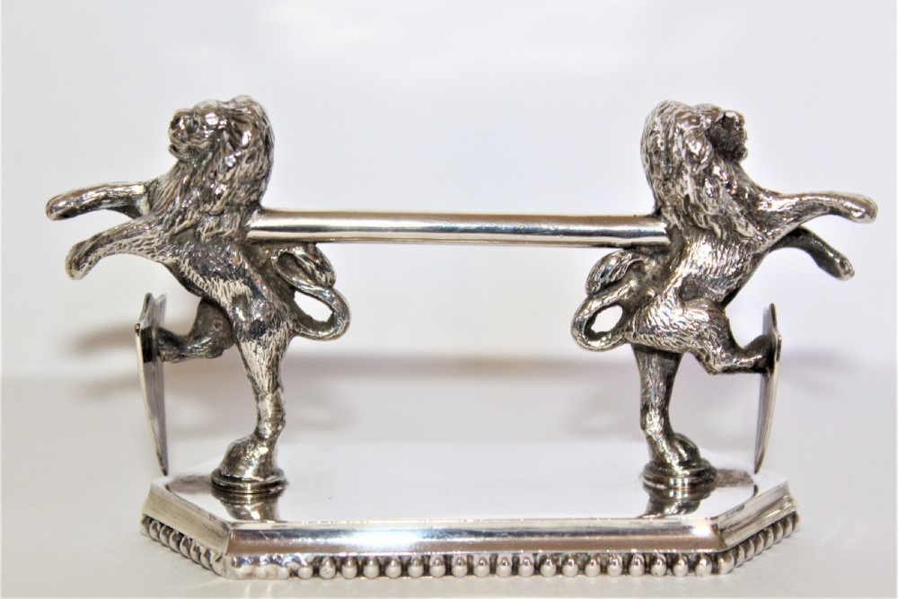 A pair of silver-plated knife rests featuring rampant lions holding shields mounted on beaded rectangular bases. View IV