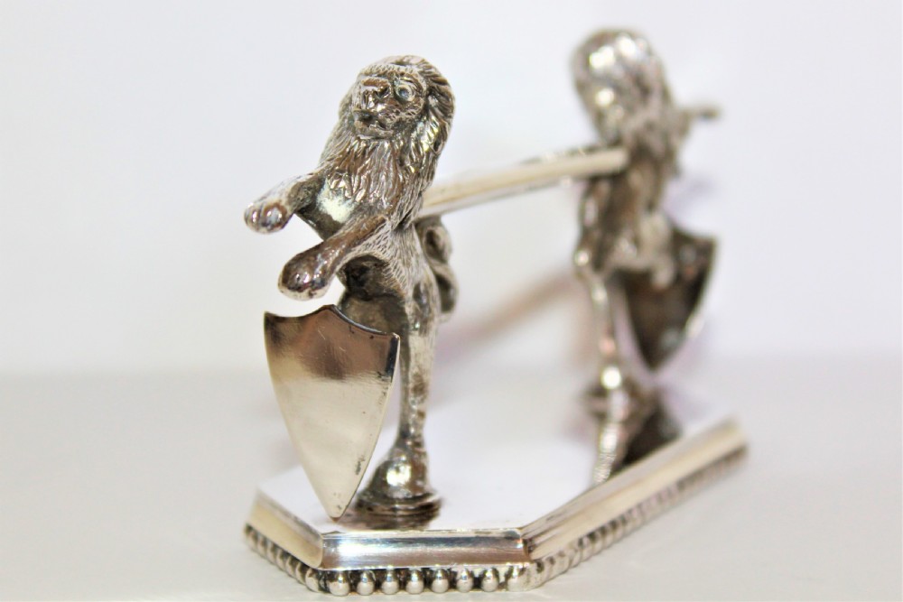 A pair of silver-plated knife rests featuring rampant lions holding shields mounted on beaded rectangular bases. View V