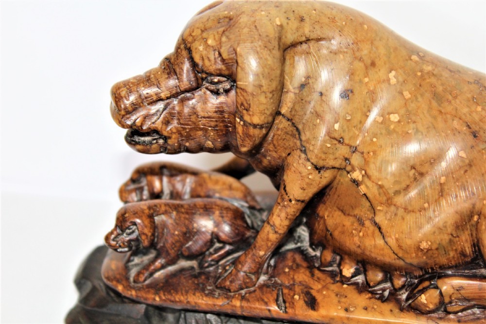 A carved warm brown soapstone sculpture depicting a sow reclining alongside her piglets on an ornate dark wooden stand. View V