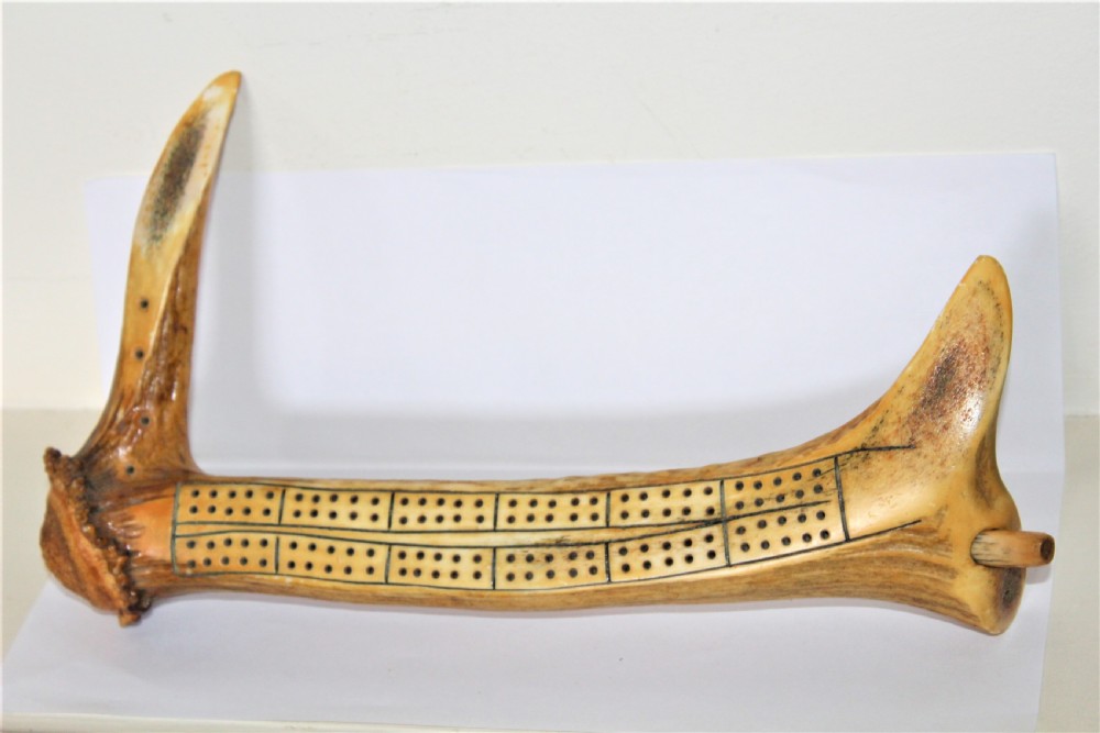 An antique cribbage board crafted from a natural stag antler featuring drilled scoring holes and incised lines.
