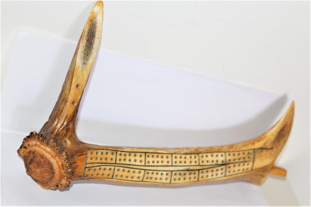 An antique cribbage board crafted from a natural stag antler featuring drilled scoring holes and incised lines. View V