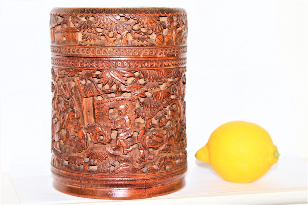 A cylindrical bamboo box covered in detailed high-relief carvings of figures and buildings. View II
