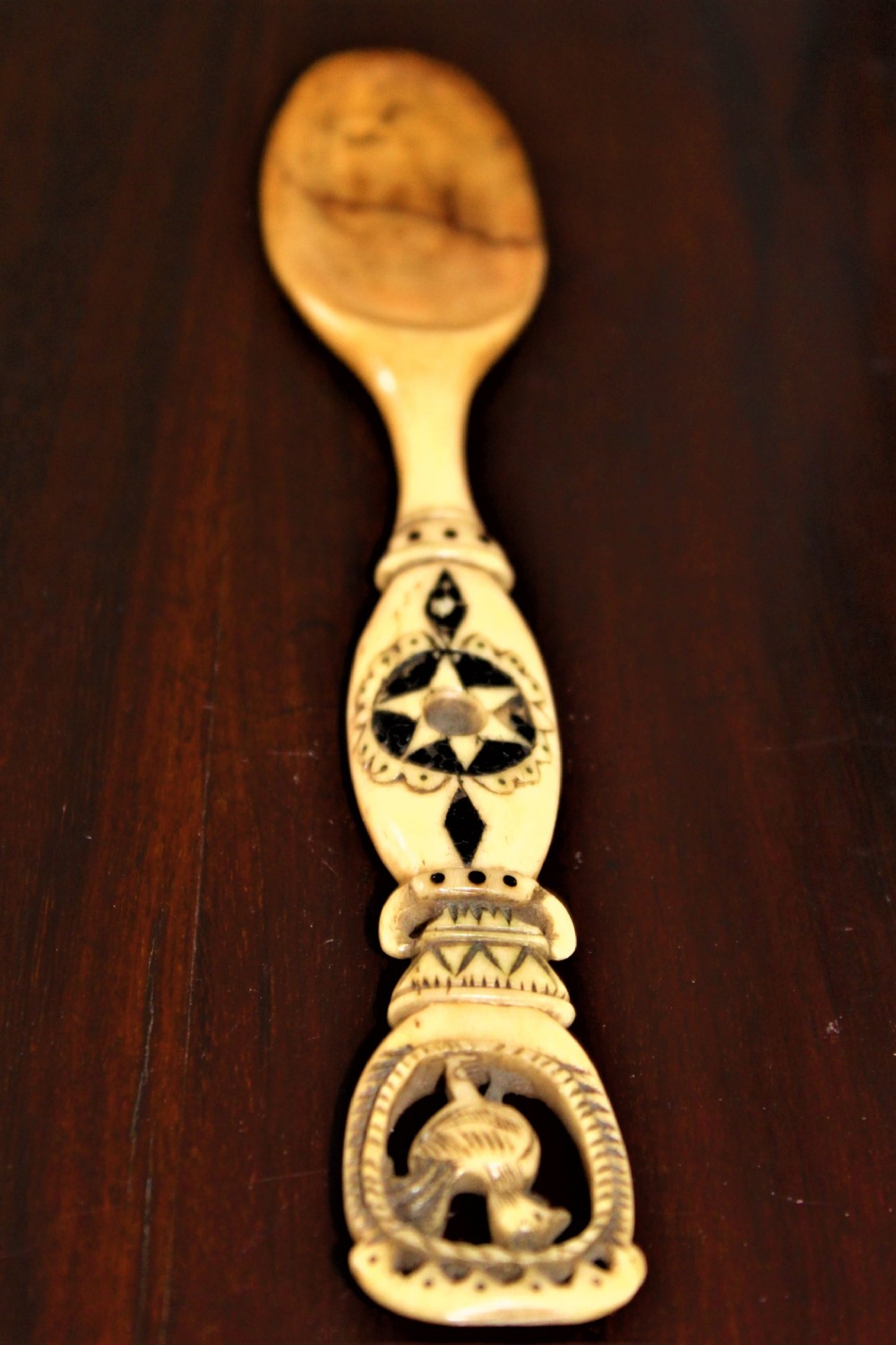 An 18th-century Central European carved stag horn love spoon featuring black geometric engravings and a bird motif cut-out on the handle.