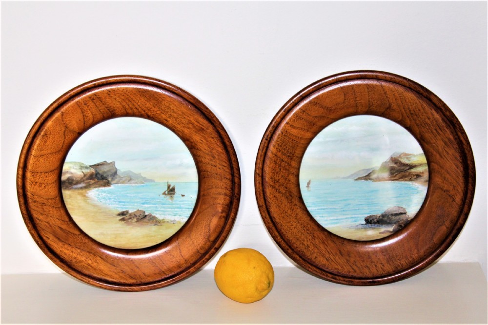 A pair of circular watercolour paintings depicting coastal landscapes with boats and cliffs, set inside polished wood circular frames. View III