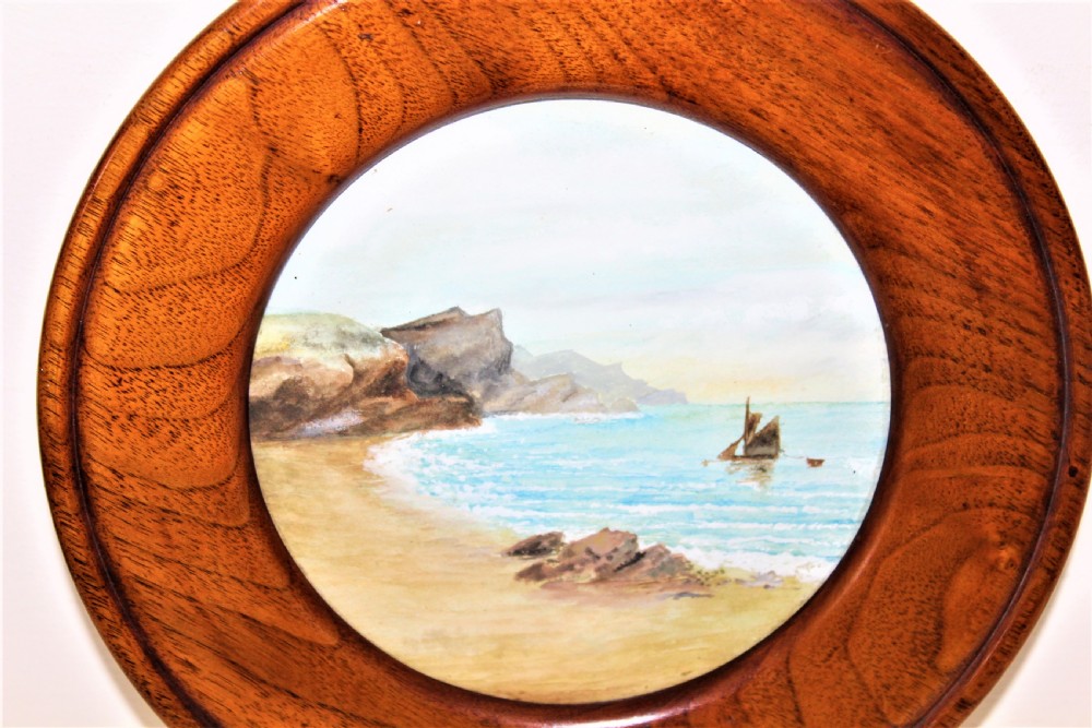 A pair of circular watercolour paintings depicting coastal landscapes with boats and cliffs, set inside polished wood circular frames. View IV