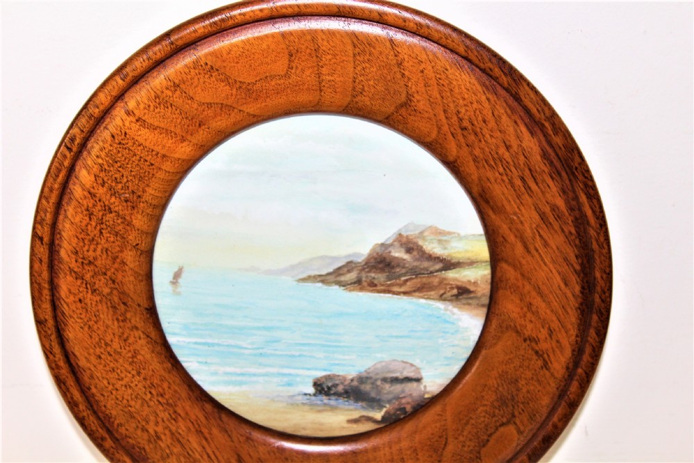 A pair of circular watercolour paintings depicting coastal landscapes with boats and cliffs, set inside polished wood circular frames. View V