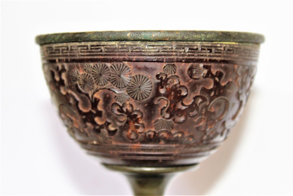 A footed Chinese goblet featuring a dark brown carved coconut shell bowl mounted on a slender pewter stem and circular base. View II