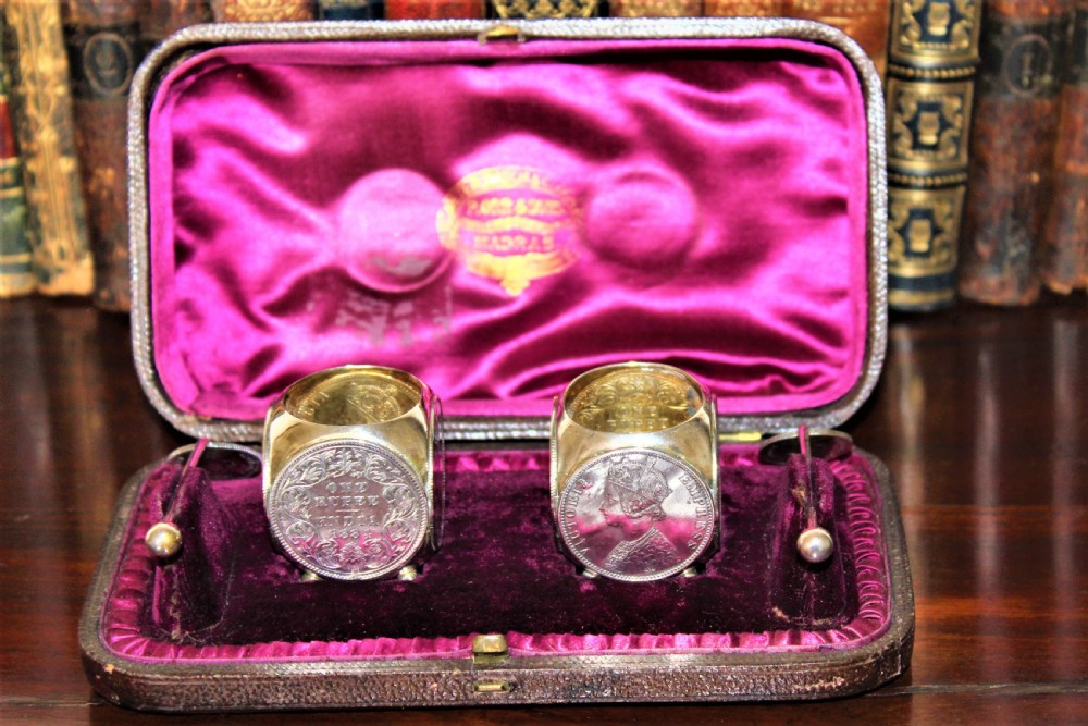 A pair of Victorian silver coin salt cellars with hinged coin lids and spoons sitting in front of an open fitted magenta velvet box. View II