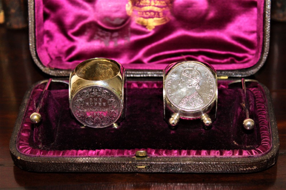 A pair of Victorian silver coin salt cellars with hinged coin lids and spoons sitting in front of an open fitted magenta velvet box. View III