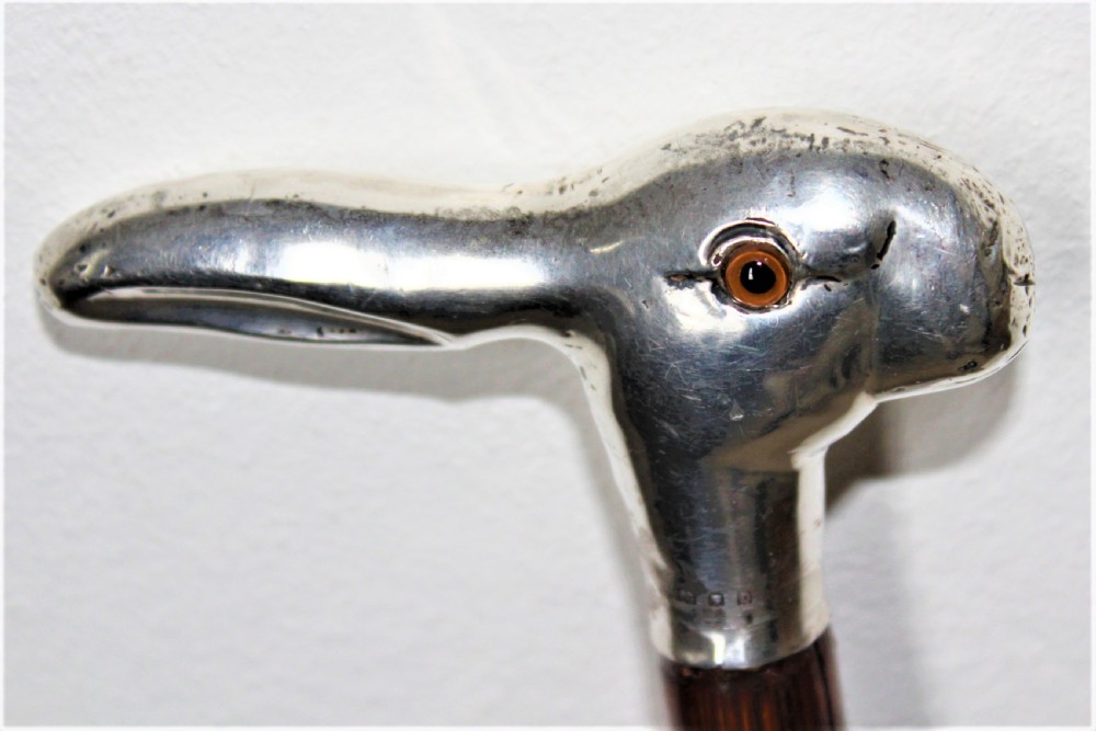 A close-up view of a silver walking stick handle shaped like a hares head with a amber-coloured glass eye and silver hallmarks. View IV