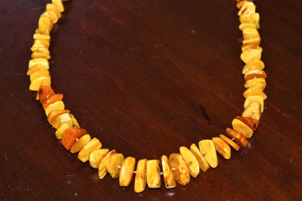 A long single strand of irregularly shaped natural amber beads displaying varied tones from pale butterscotch to warm golden honey. View V