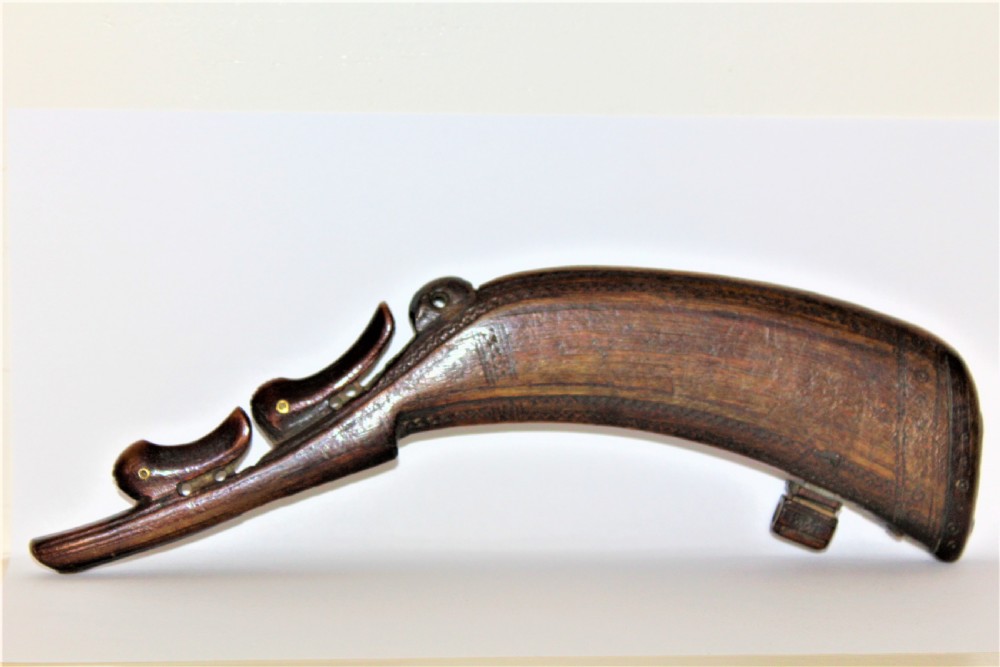 A curved 18th-century carved dark horn powder flask featuring decorative zoomorphic terminal detailing and brass eye inserts.