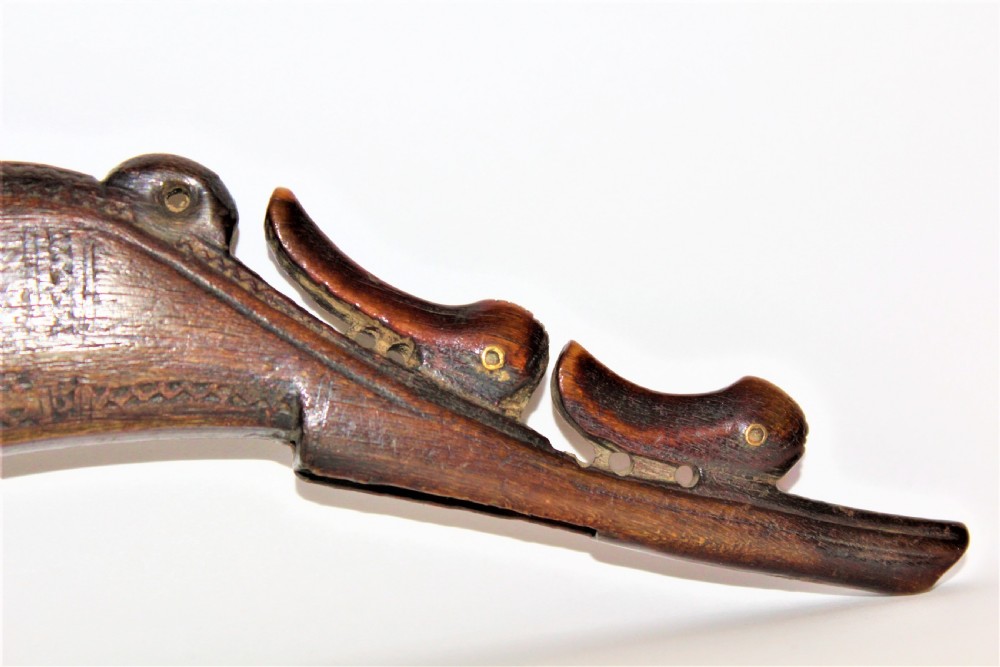 A curved 18th-century carved dark horn powder flask featuring decorative zoomorphic terminal detailing and brass eye inserts. View II