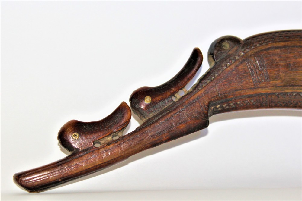 A curved 18th-century carved dark horn powder flask featuring decorative zoomorphic terminal detailing and brass eye inserts. View IV