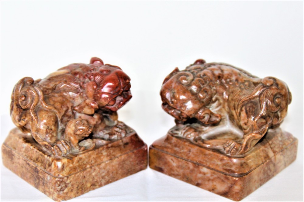 A pair of carved brown and red soapstone desk seals featuring Chinese guardian lions mounted on square plinths.