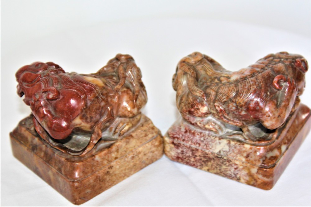A pair of carved brown and red soapstone desk seals featuring Chinese guardian lions mounted on square plinths. View II
