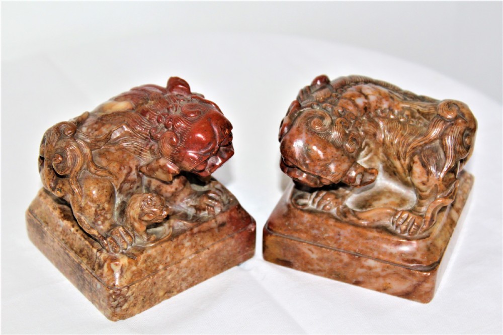 A pair of carved brown and red soapstone desk seals featuring Chinese guardian lions mounted on square plinths. View V