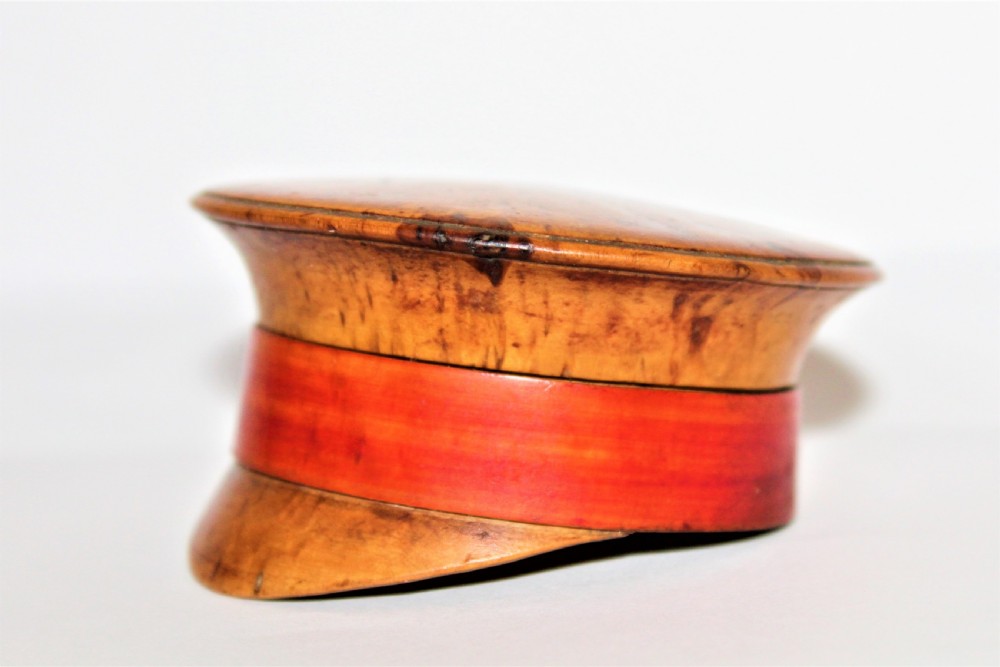 A small turned burr walnut novelty snuff box shaped like a military cap featuring a red painted central band. View II