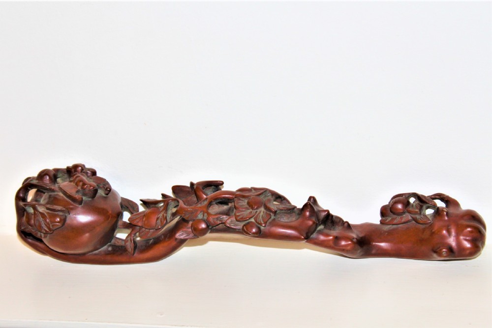 A hand-carved boxwood Ruyi sceptre featuring naturalistic branches, leaves, and peach motifs.