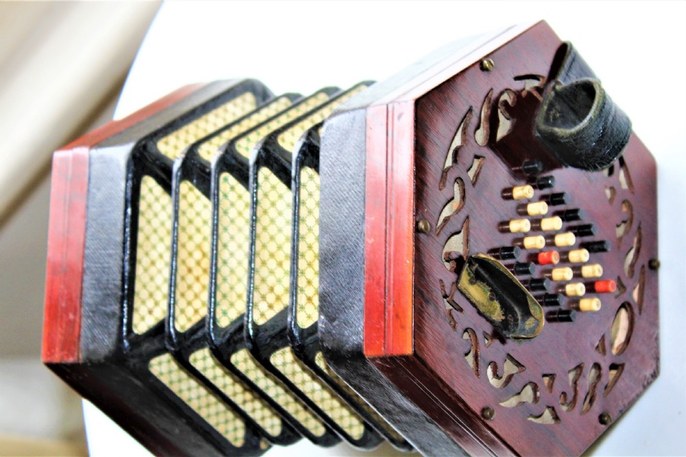 A Victorian hexagonal Lachenal button concertina featuring pierced rosewood fretwork, multi-fold leather bellows with printed paper design, and bone buttons.