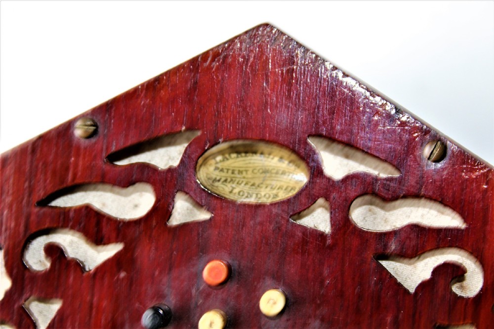 A Victorian hexagonal Lachenal button concertina featuring pierced rosewood fretwork, multi-fold leather bellows with printed paper design, and bone buttons. View V
