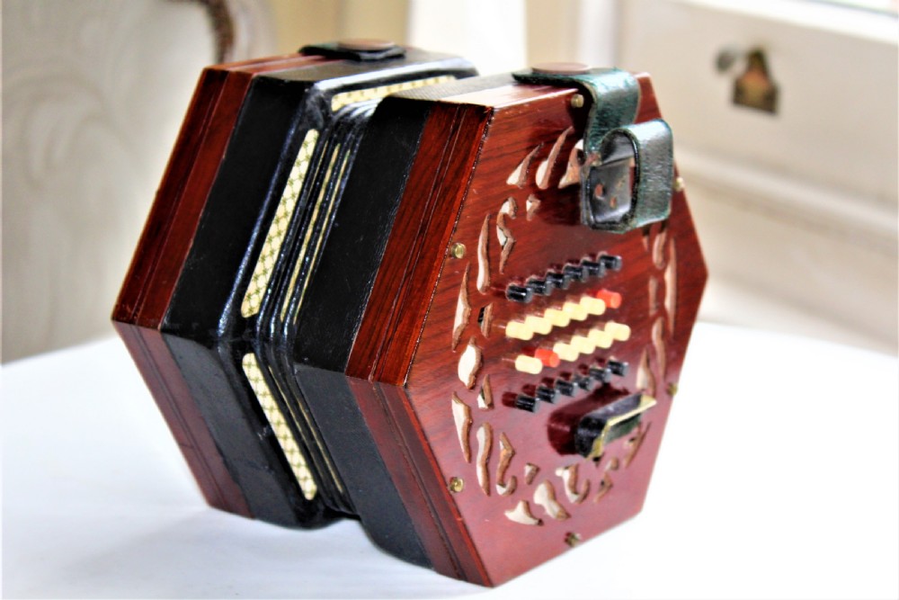 A Victorian hexagonal Lachenal button concertina featuring pierced rosewood fretwork, multi-fold leather bellows with printed paper design, and bone buttons. View VI