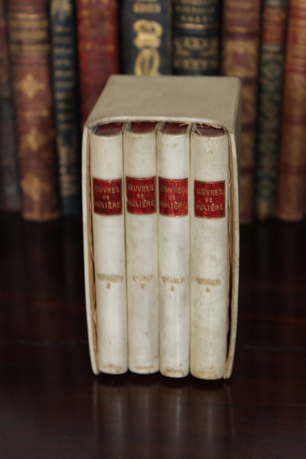 A four-volume set of small antique books bound in cream vellum with red gilt-tooled spine labels, housed inside a matching vellum slipcase.