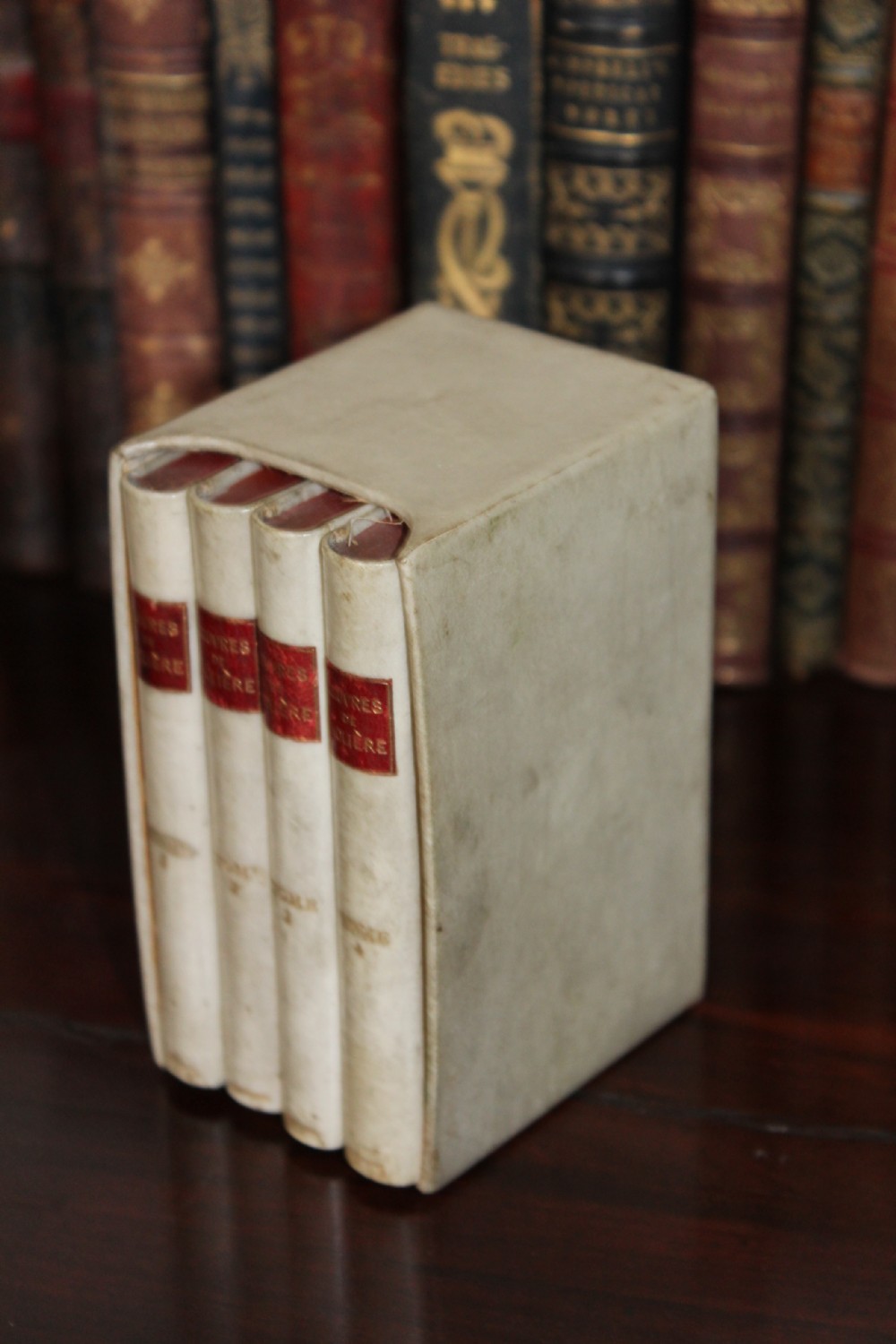 A four-volume set of small antique books bound in cream vellum with red gilt-tooled spine labels, housed inside a matching vellum slipcase. View II